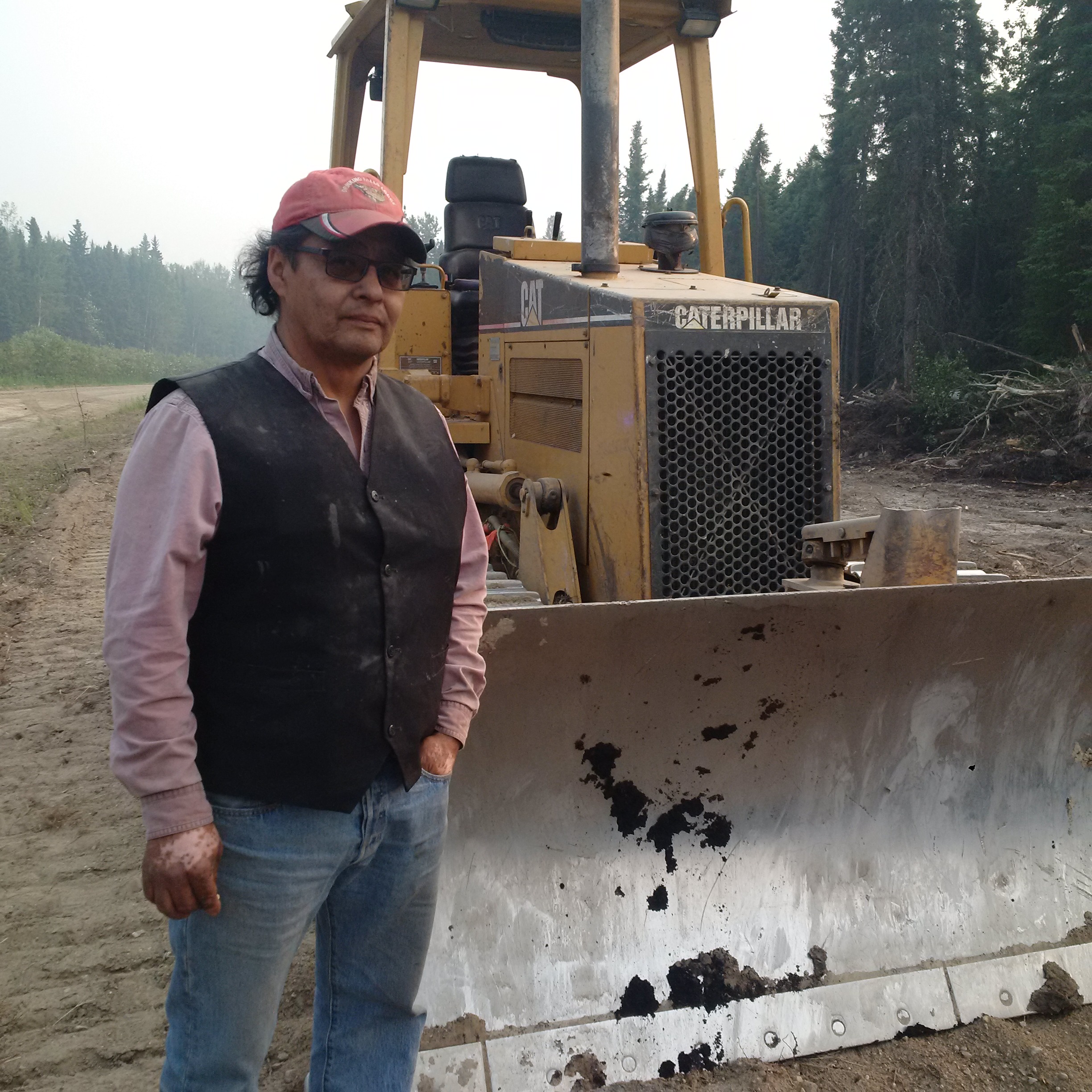 Lionel Bird stands by his bulldozer he's been using to build firewalls. Bird says province making a mistake restricting night firefighting. (APTN/Photo)