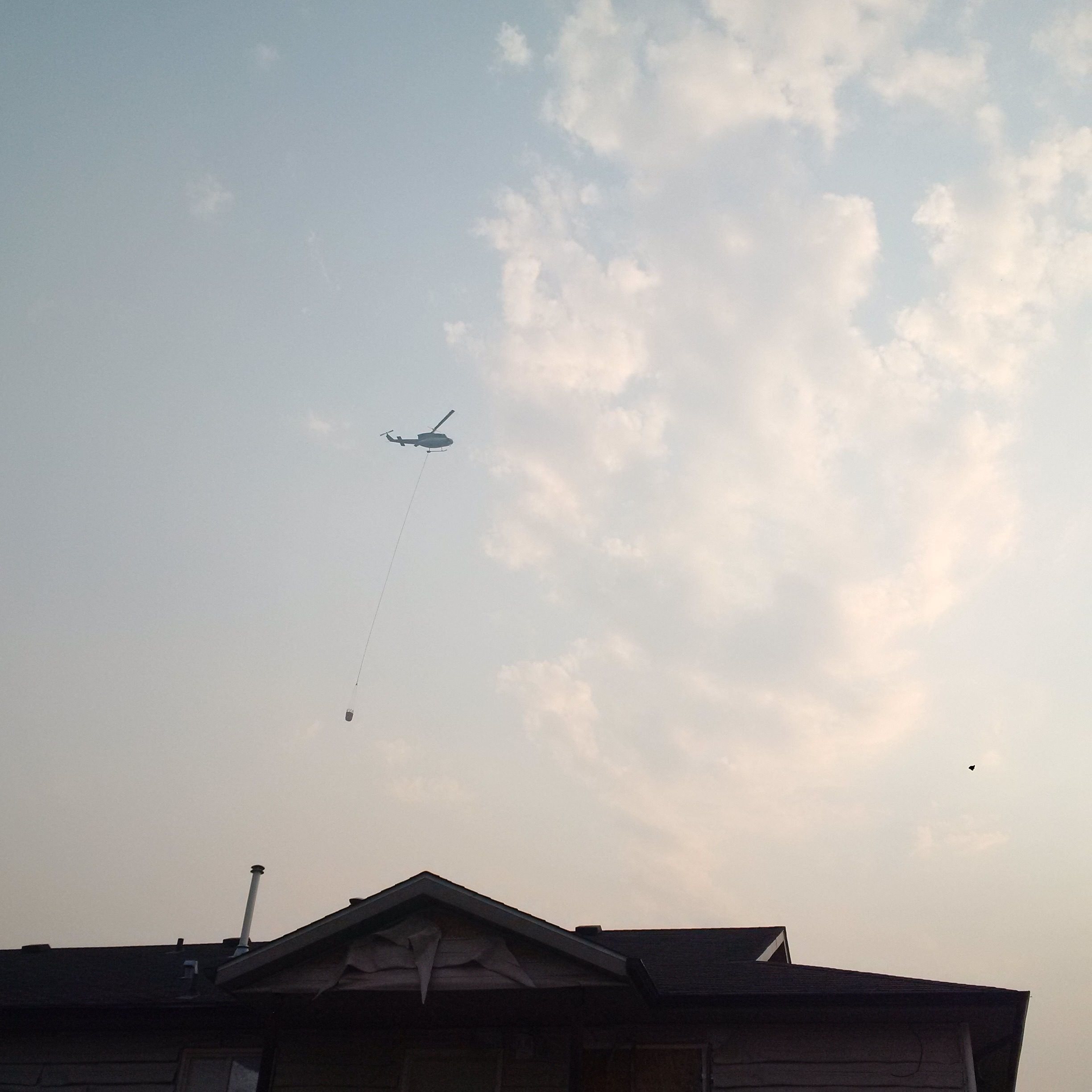 A helicopter with a water payload flies over Montreal Lake on the way to douse wildfire. (APTN/Photo)