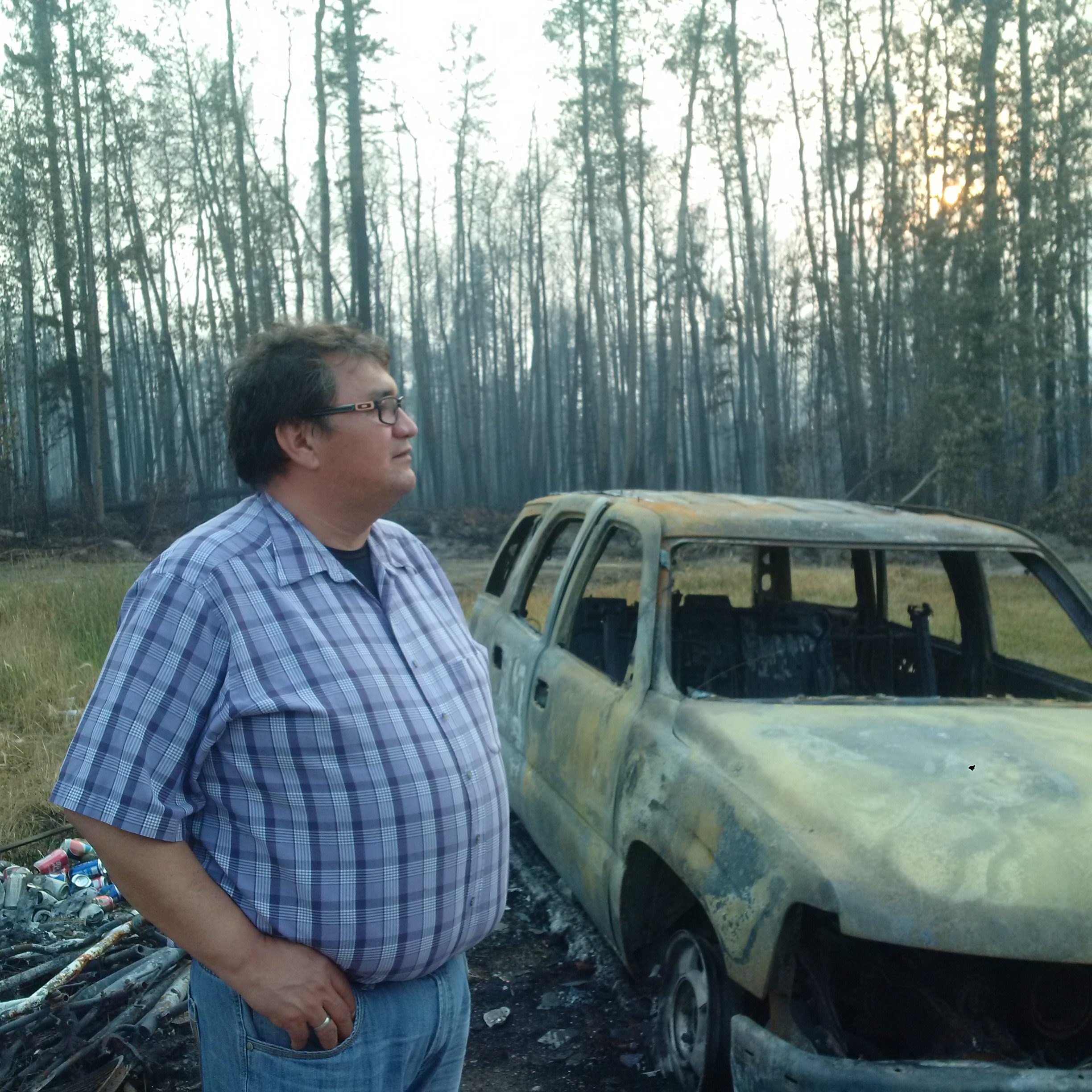 Montreal Lake Chief Edward Henderson stands beside the charred remains of a car in the backyard of a Montreal Lake home. (APTN/Photo)